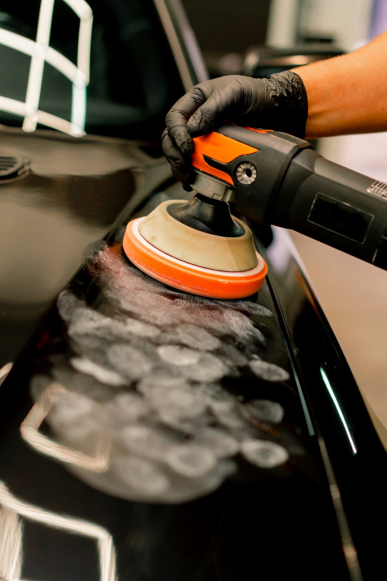 Close-up of a car wash worker using a polishing machine to polish the hood of black luxury car